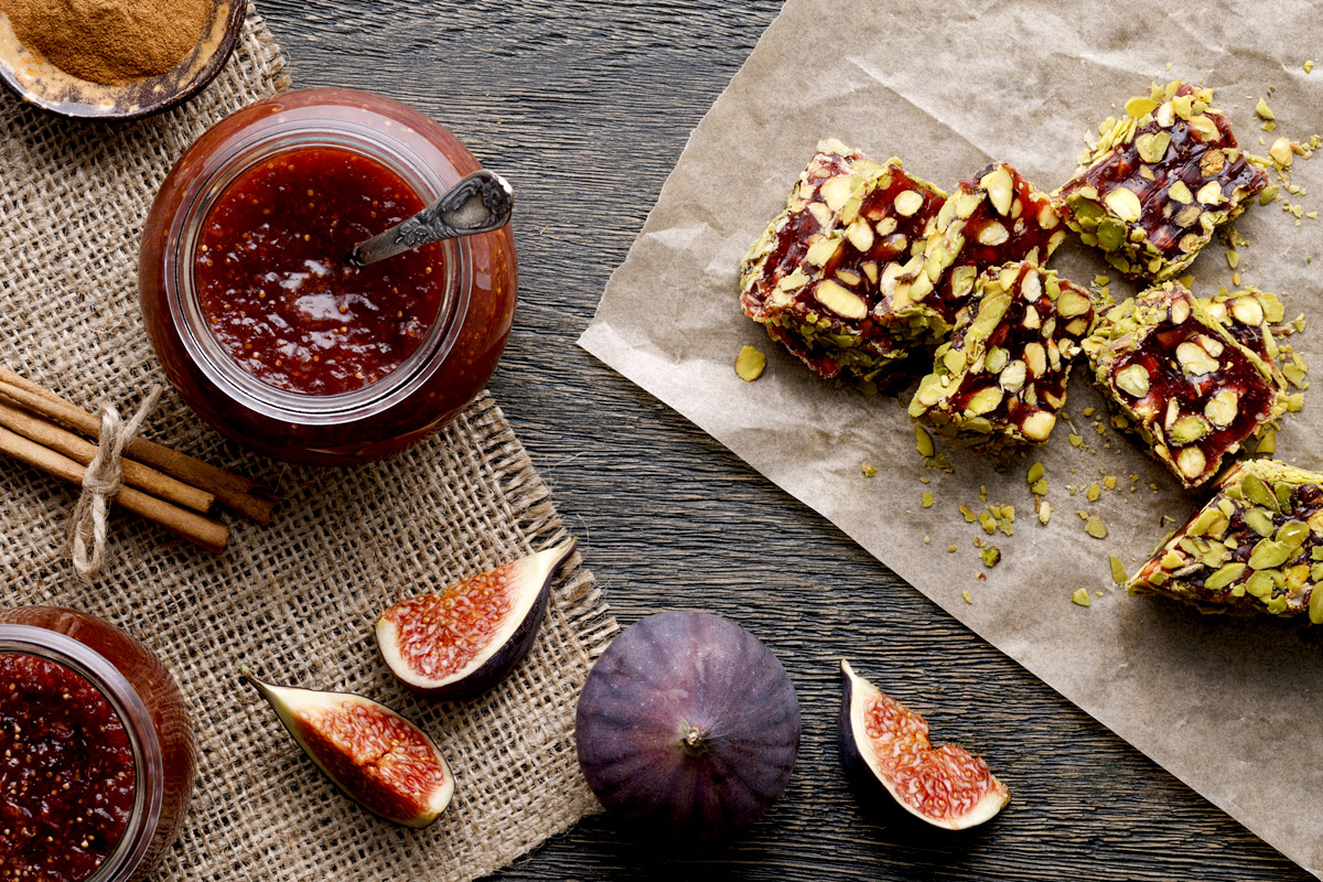 Glass jar with some fig jam and fig turkish delight with pistachio nuts on a dark wooden background.